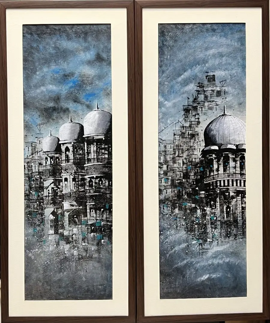 Two vertical paintings depicting cityscapes with buildings and domes. The buildings are in a muted blue and gray color palette, with a cloudy sky in the background. The paintings are framed in brown wood.