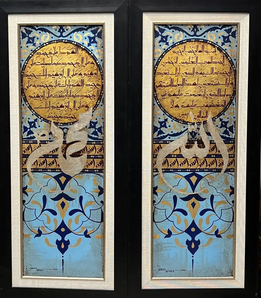 Two vertical paintings featuring intricate Arabic calligraphy and decorative patterns in shades of blue, gold, and white. The paintings are framed in black wood.